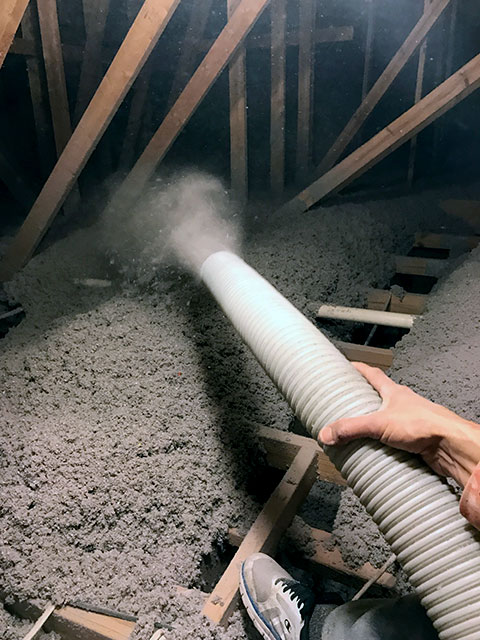 Technician's hand holding hose as new insulation is added to attic after waste removal and clean up